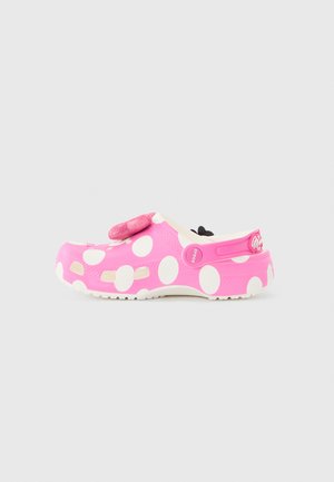 Zoccolo slip-on rosa con grandi pois bianchi, cinturino regolabile al tallone e decorazione con fiocco rosa glitterato sulla parte superiore.