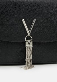 Svart texturerad läderväska med en framträdande silver "V"-logotyp, metallkedjetofs och en elegant klaffstängning.