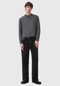 Grå langærmet polo med krave, kombineret med sorte jeans med lige ben. Har et diskret logo på brystet og en tekstureret stof.