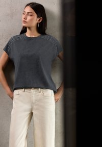 Top gris de manga corta con acentos de tachuelas en los hombros, combinado con pantalones de talle alto en un tono beige claro. Textura suave y corte relajado.