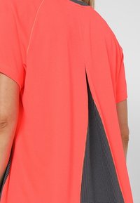 Korálová blůza s krátkými rukávy a rozparkem na zádech. Obsahuje kontrastní podšívku s černobílým vzorem. Hladká textura, lehký materiál.