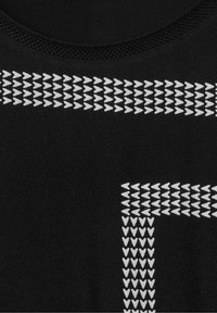 Haut de sport noir en tissu texturé, avec un col rond et des motifs en flèche argentés au niveau de la poitrine et des épaules.