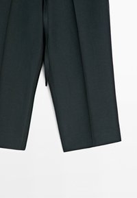 Zbliżenie czarnych spodni o prostych nogawkach z przednim środkowym zagnieceniem na jednolitym białym tle.