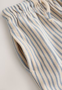 Close-up of beige fabric pants with vertical blue stripes and an elastic waistband with a drawstring.