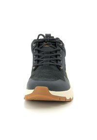 Zapato deportivo masculino negro con parte superior de malla texturizada, cordones planos, suela de goma y acentos en tono marrón que contrastan en el talón y la suela.