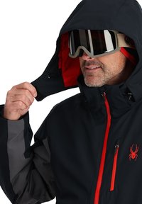 Black waterproof jacket with red accents and lining. Features a zipper front, adjustable hood, and logo on the chest. Includes grey sleeve panels.