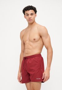 Shorts de bain rouges en tissu lisse avec une taille élastique et un cordon de serrage. Caractérisés par un logo blanc Calvin Klein sur le devant.
