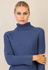 Maglione a collo alto a coste in blu profondo, con un design aderente, maniche lunghe e un colletto alto. Tessuto morbido con finiture senza cuciture.