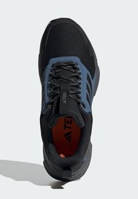 Czarne buty sportowe z niebieskimi akcentami, teksturowana siateczka wierzchnia, sznurowadła, wyściełany kołnierz i pomarańczowe wnętrze. Logo widoczne na języku i bokach.
