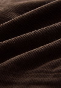 Brązowa tkanina sztruksowa z delikatnymi pionowymi prążkami i miękką fakturą, prezentująca faliste fałdy i subtelny połysk.