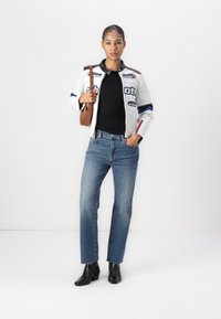 Casaco de pele branco com realces coloridos, blusa preta justo, jeans de perna reta azul claro e botins pretos de salto. Mala castanha de ombro.