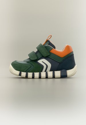 Baskets pour enfants avec empiècements verts, bleu marine et orange, deux bandes velcro, semelle blanche et détail graphique sur le côté, sur fond neutre.