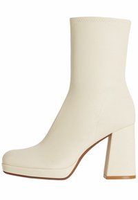 Bota de tobillo en color crema con un diseño elegante, puntera cuadrada, tacón grueso y textura suave. Presenta costuras mínimas y un acabado brillante.