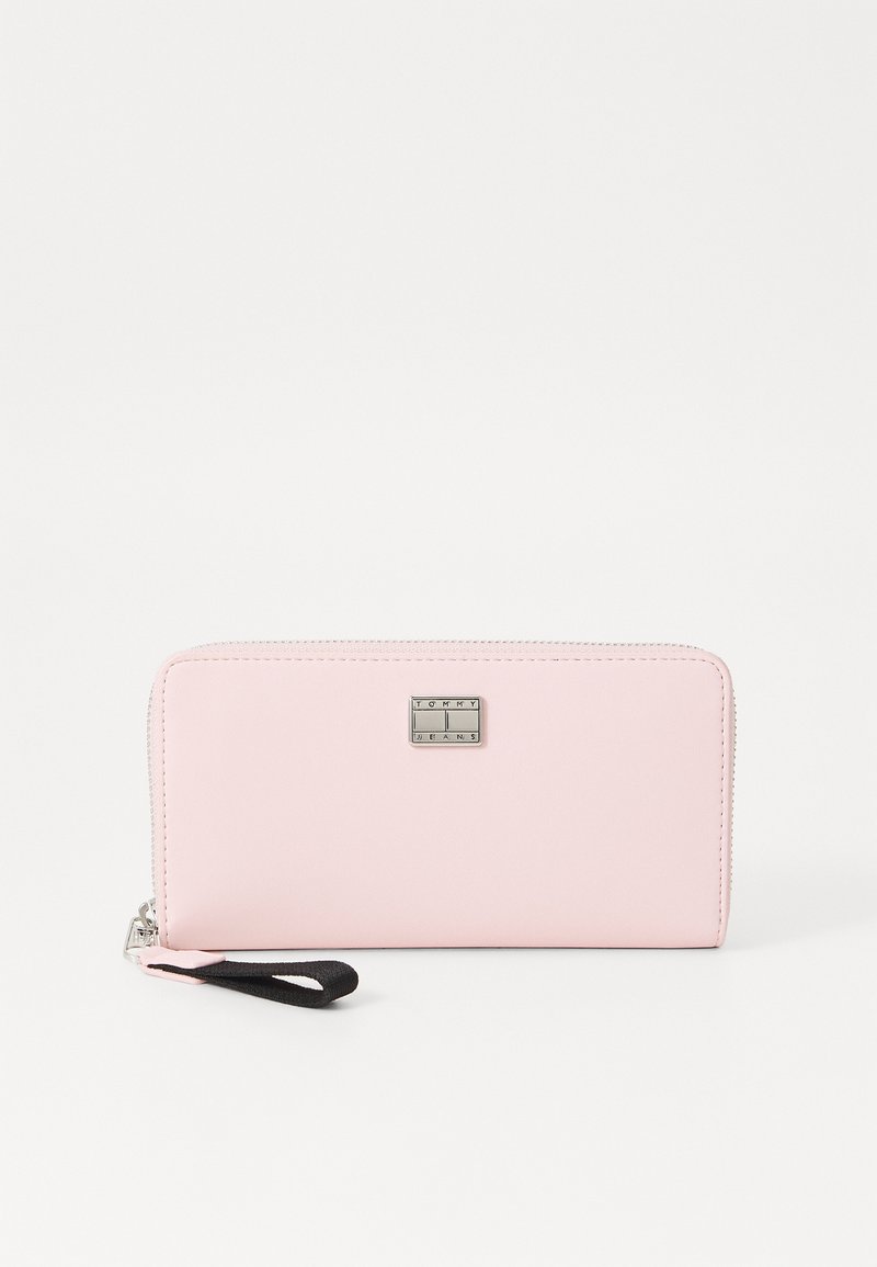 Portafoglio rosa con zip in materiale sintetico liscio. Presenta una placca logo argentata e un cinturino da polso nero. Design pulito e minimalista.