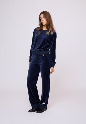 Navyblauw velours trainingspak met lange mouwen, elastische manchetten en een sweatpants ontwerp met zijzakken en gouden strikaccenten.