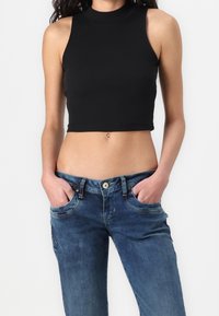 Crop top nero a coste con collo alto e design senza maniche, abbinato a jeans in denim blu con chiusura a bottone e tasche frontali.