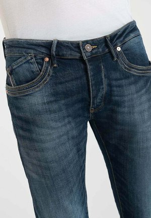 Donkerblauwe denim jeans met een klassiek vijf-pocket ontwerp, koperen hardware en contrasterende stiksels. Slim fit met lichte vervaging op de dijen.