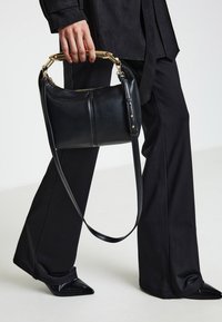 Borsa a mano in pelle nera con dettagli in oro. Presenta una forma curva, una tracolla regolabile e una chiusura con cerniera. Texture liscia e finitura lucida.