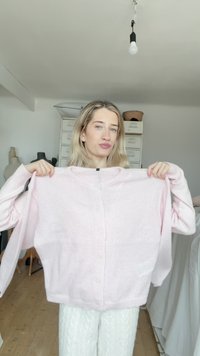 Svetloružový, veľký kardigán z mäkkého materiálu s okrúhlym výstrihom, dlhými rukávmi a piatimi gombíkmi vpredu.