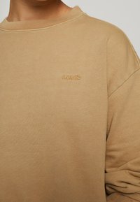 Sweatshirt beige en coton doux, avec un col côtelé et un logo "Levi's" discret en relief sur la poitrine. Coupe décontractée avec des manches amples.