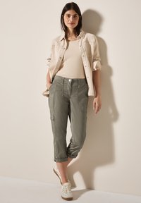 Ljusbeige denimskjorta, figurnära khakibyxor med fickor, vända ärmslut och knappstängning. Vita sneakers fulländar outfiten.