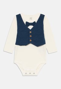Cremfarbener Babyschlafi mit langen Ärmeln und angenähter dunkelblauer Weste, drei vorderen Holzknöpfen und passender dunkelblauer Fliege am Halsauschnitt.