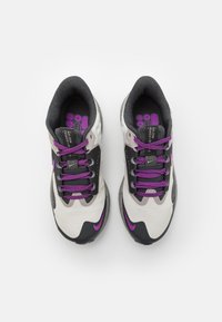 Idrottsskor med en överdel i grå och vit mesh, lila detaljer, platta snören och en texturerad svart sula. Har en vadderad krage.