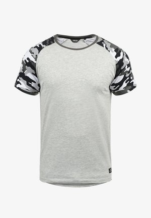 Grå T-skjorte med korte ermer som har et svart og hvitt camouflasjemønster på skuldrene. Laget av et mykt, lett stoff.