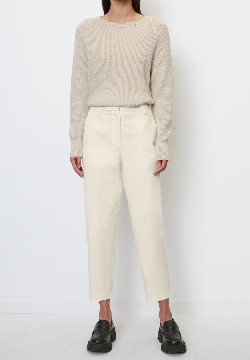 Beige Strickpullover mit runder Ausschnitt, kombiniert mit cremefarbenen, schmal zulaufenden Hosen. Das Model trägt schwarze Plateauslipper.