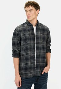 Rutet skjorte i mørkeblå og grå, lavet af flannel. Har knaplukning foran, lange ærmer og en brystlomme. Bæres med denim jeans.