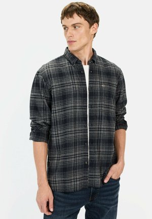 Plaid shirt in dark blue and gray, made of flannel. Features button-up front, long sleeves, and a chest pocket. Worn with denim jeans.