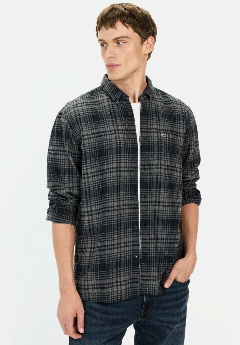 Rutet skjorte i mørkeblå og grå, lavet af flannel. Har knaplukning foran, lange ærmer og en brystlomme. Bæres med denim jeans.