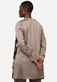 Beżowa tunika z długim rękawem o jedwabistej fakturze, ozdobiona kwiatowym wzorem po bokach, z prostym okrągłym dekoltem.