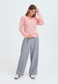 Pull en tricot rose pâle avec col en V, manches longues ; associé à un pantalon gris ample et des baskets blanches. Texture lisse, coupe décontractée.