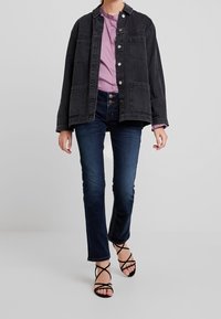 Svart denimjacka med två framfickor, tillsammans med en ljusrosa topp, mörkblå utsvängda jeans och svarta remsandaler.