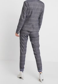 Grå rutigt kostym med skräddarsydd jacka och slim-fit byxor. Beaktansvärda vita knapprack på ärmarna, textilerad tyg och randiga ankeln detaljer.