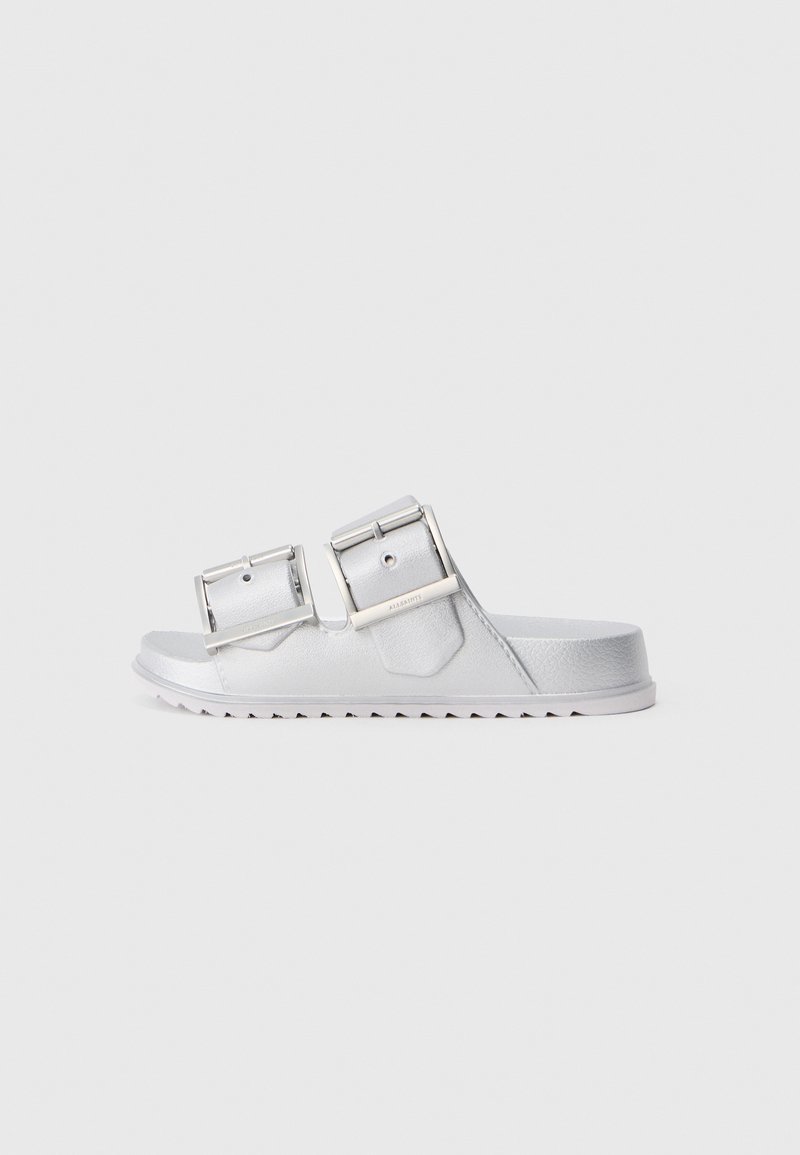 Sandalias plateadas con dos correas anchas ajustables, material texturizado y una suela plana con un patrón en zigzag en la parte inferior.
