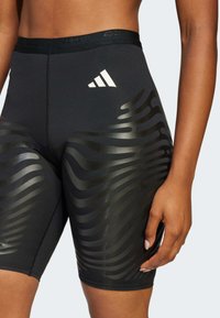 Crne atletske kratke hlače s sjajnim uzorkom valova s bočne strane. Elastični pojas s ADIZERO brendiranjem. Glatka, oblikovana tkanina.