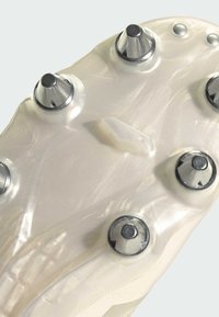 Skor med en genomskinlig vit sula, som har metalliska silvernubb och en texturerad yta för grepp och stabilitet.