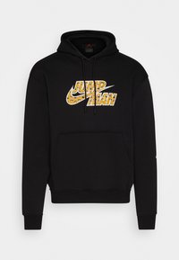 Sort hættetrøje med stor, mønstret Nike-logo i gul med dyreprint. Inkluderer justerbare snore og en frontlomme.