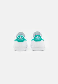 Weisse Leder-Sneaker mit einer türkisfarbenen Fersenkappe, mit "stan smith" Branding und einer strukturierten Gummisohle. Rückansicht.