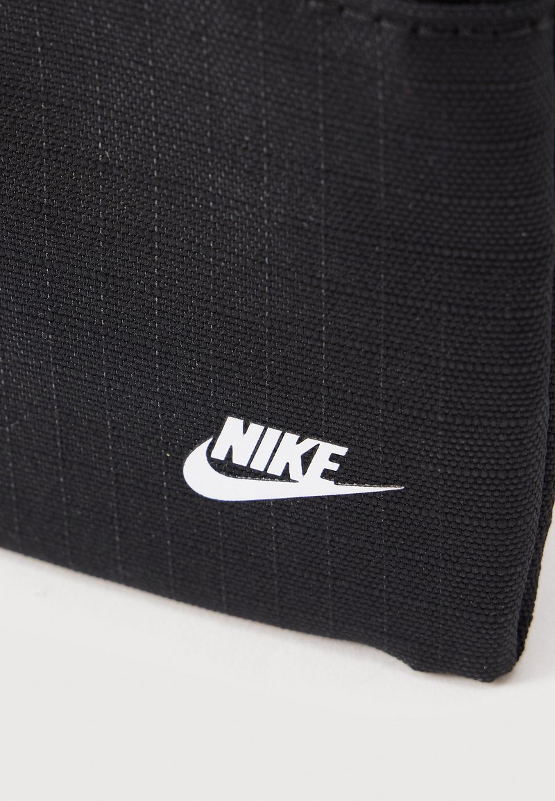 Cartera de tela negra con textura que presenta el logo blanco de Nike y el símbolo swoosh sobre un fondo plano y claro.