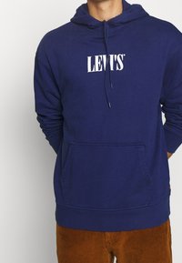 Felpa con cappuccio di un blu scuro, realizzata in cotone, dotata di tasca frontale, cappuccio con cordino regolabile e logo bianco "LEVI'S" stampato sul petto.