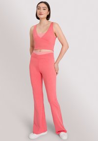 Roze crop top met een wikkeldesign, gecombineerd met flared roze broek. Beide items zijn gemaakt van een gladde stof en hebben een aansluitende snit.