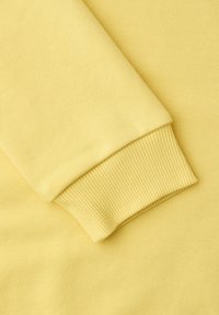 Manche de sweat-shirt jaune repliée sur le corps du vêtement, présentant un poignet côtelé et une texture de tissu en coton lisse.