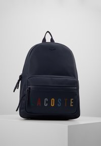 Navy blue reppure backpack with front zip pocket featuring multi-colored "LACOSTE" lettering and a small crocodile logo on top center.