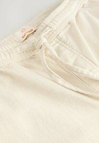 Shorts à cordon de serrage de couleur crème, fabriqués en tissu doux. Présentent une étiquette avec "Next Supply" et des détails de couture le long de la taille.