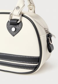 Geantă de mână din piele albă cu accente negre, formă rotunjită, cusături contrastante, accesorii în formă de inimă și închidere cu fermoar. Potrivită pentru utilizarea zilnică.