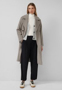 Manteau en laine gris avec un col oversize, boutons double boutonnage ; superposé à un pull gris clair et un pantalon large noir ; baskets beiges.