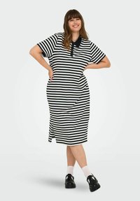 Pruhované černobílé šaty s krátkými rukávy a límečkem, volnějšího střihu a s postranním rozparkem. Nošeno s černými botami a bílými ponožkami.